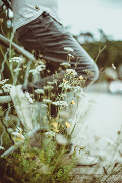 Side view low section of a man in jeans leaning against a metal fence in a park surrounded by wildflowers, Luxembourg