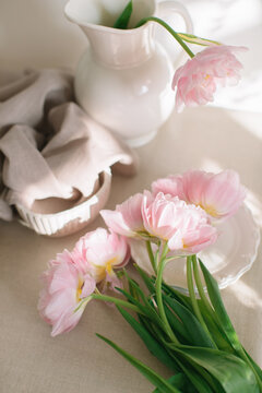 Close-up overhead view of a bouquet of Pink peony tulips (double tulips) on a table with assorted crockery in sunlight
