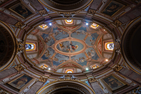 View of the ornate frescoed dome of the Basilica of Our Lady of Mount Carmel with intricate religious paintings and golden architectural details in Valletta, Malta.