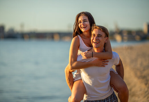 Happy couple enjoying piggyback ride on beach.