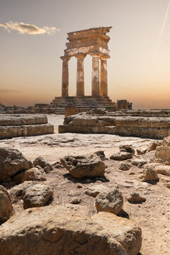 View of the ancient Temple of Castor and Pollux with its standing Doric columns and scattered stone ruins under a warm sunset sky in the Valley of the Temples, Agrigento, Sicily, Italy.