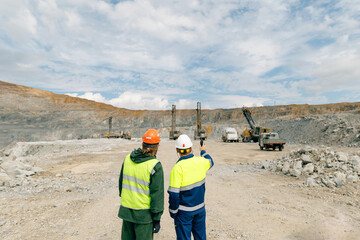 Two workers discussing excavation at open pit mine, gold mining industry