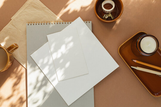Overhead view of blank paper, cards and notepad on a desk with a cup of coffee, scented block candle and assorted stationery on a sunny day