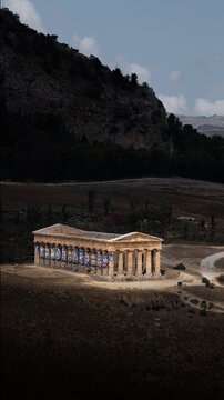View of the ancient Doric Temple of Segesta nestled in a rugged landscape with rolling hills and dark green trees under a cloudy sky Segesta, Sicilia, Italy.