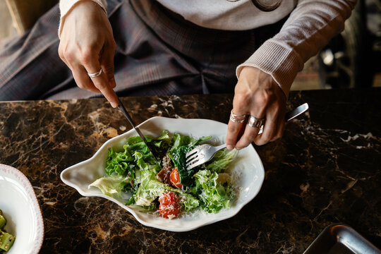 Close-up of Woman sitting at a table eating a fresh tuna salad with tomatoes and grated cheese