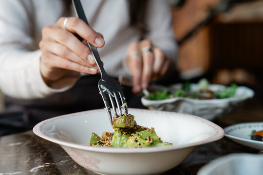 Close-up of Woman sitting at a table Eating an Asian style Avocado Salad with soy sauce and Sesame Seeds