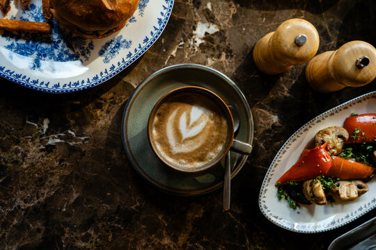 Overhead view of a cappuccino with a Gourmet Beef Cheeseburger with Crispy Sweet Potato Fries and mixed roasted vegetables