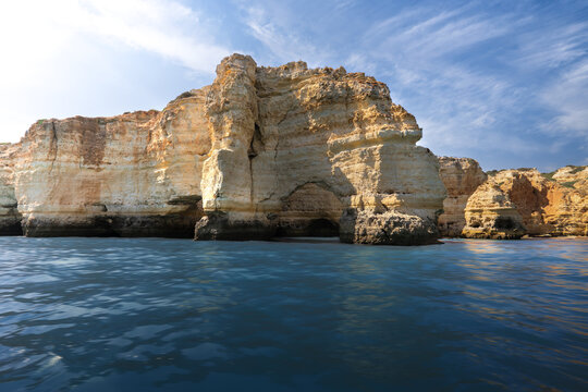 View of dramatic limestone cliffs and sea caves rising from the turquoise Atlantic Ocean under a bright blue sky Portimao, Faro District, Portugal.