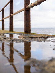 Fototapeta premium Rusty railing along the coast with reflections in puddles.