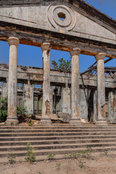 View of the crumbling neoclassical ruins of a colonial building with stone columns and a pediment under a clear blue sky in Bijagos, Guinea Bissau.