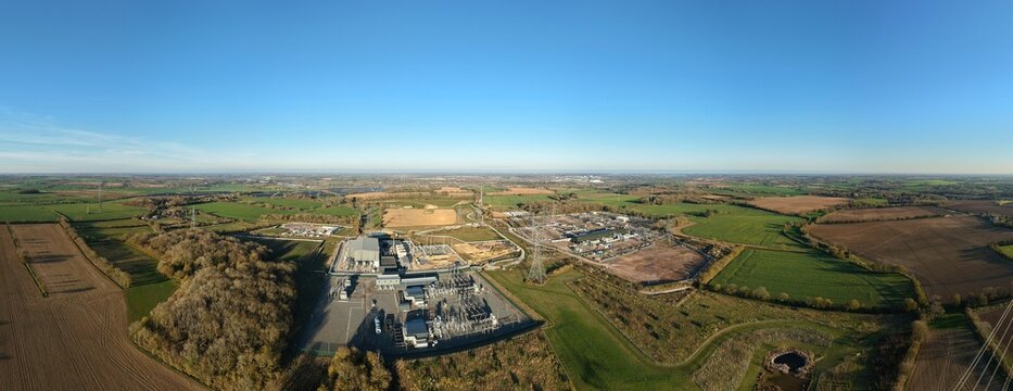 Aerial view of the National Grid Bramford Substation juxtaposed against the patchwork of green fields under a vast blue sky, Ipswich, United Kingdom.