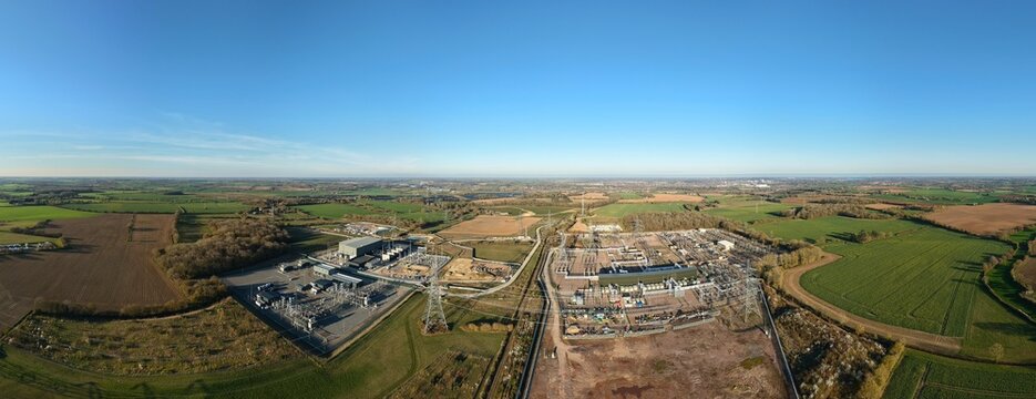 Aerial view of National Grid Bramford Substation, where steel structures meet the green fields under a vast blue sky, Ipswich, United Kingdom.