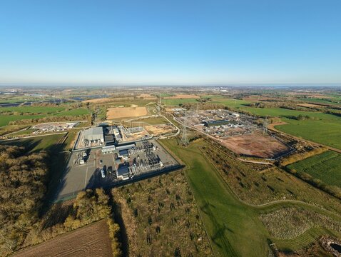 Aerial view of the National Grid Bramford substation juxtaposed against the surrounding verdant fields under a vast blue sky, Ipswich, United Kingdom.