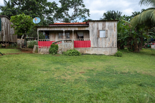 View of a traditional wooden house with a red fence and a satellite dish surrounded by lush tropical vegetation in Sao Tome and Principe.