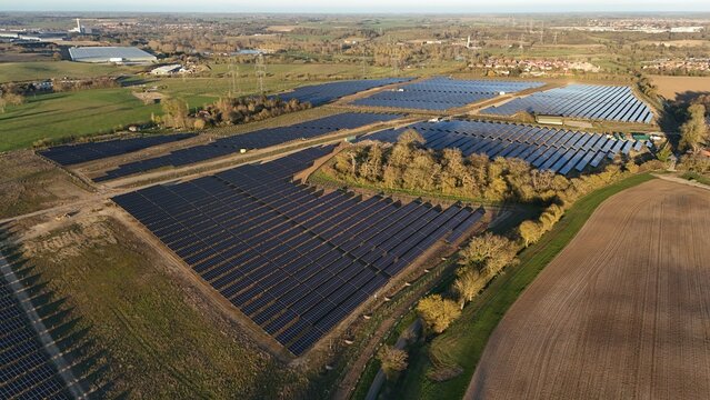 Aerial view of solar panels gleaming under the afternoon sun, juxtaposed against the green fields and buildings in the distance, Tye Lane, Ipswich, United Kingdom.