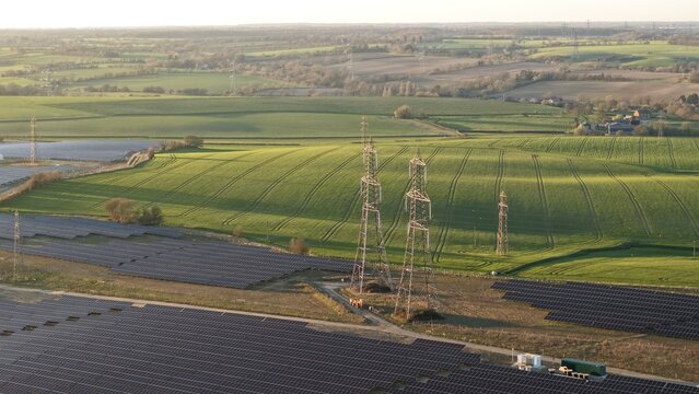 Aerial view of the Tye Lane Solar Farm, where dark panels contrast with the vibrant green fields under the soft glow of the sun, Ipswich, United Kingdom.
