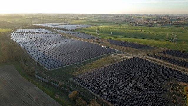 Aerial view of solar panels reflecting the sky, creating a mosaic of light and shadow amidst the green fields of Tye Lane Solar Farm, Ipswich, United Kingdom.