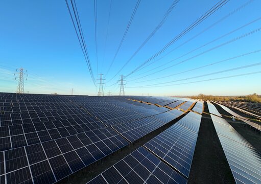 Aerial view of rows of dark solar panels contrasting with the vibrant blue sky and distant power lines at Tye Lane Solar farm, Ipswich, United Kingdom.