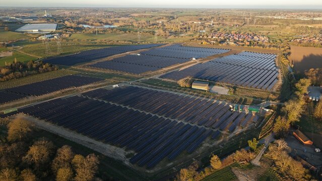 Aerial view of solar panels soaking up the sun's rays amidst the verdant fields, creating a stark contrast with the adjacent buildings, Tye Lane, Ipswich, United Kingdom.