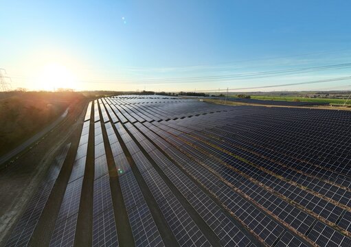 Aerial view of rows of solar panels gleam under the morning sun, contrasting with the dark panels, Tye Lane, Ipswich, United Kingdom.