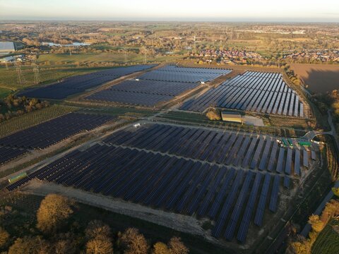 Aerial view of solar panels basking in the golden sunlight, reflecting the clear sky above, contrasted by the surrounding green fields, Tye Lane, Ipswich, United Kingdom.