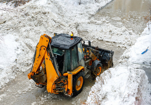 Heavy industrial machinery cleaning melting ice and snow piles.
