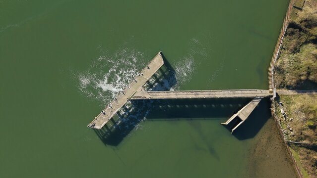 Aerial view of the stark concrete structure piercing the water, creating turbulent patterns against the calm green surface, Ipswich, United Kingdom.
