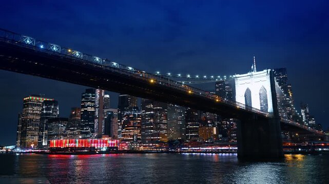 The Brooklyn Bridge with bright illumination at night. New York City skyline with street lights from river.
