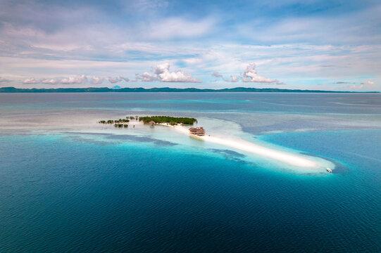 Aerial view of a pristine sandbar stretches out from a verdant island, fringed by turquoise shallows and deep blue ocean under a sky of scattered clouds, Mobo, Bicol, Philippines.