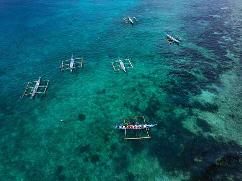 Aerial view of outrigger boats floating on the turquoise water reflecting the sky above, creating a mesmerizing contrast of blues and greens, Oslob, Cebu, Philippines.
