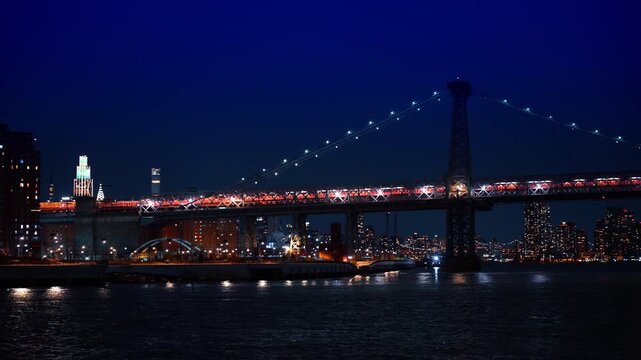Lights illuminate beautiful Williamsburg Bridge at night. Travel by the East River in New York, USA.