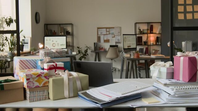 Zoom out no people shot of white office desk featuring open laptop, colourful gift boxes and piles of business documents