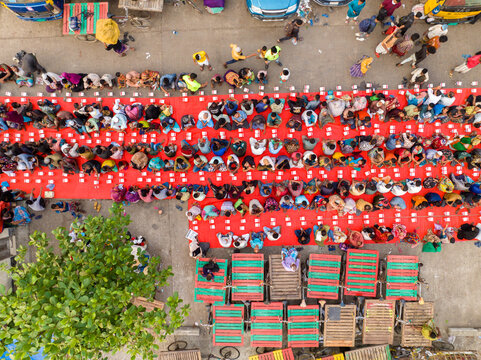 Dhaka, Bangladesh - 17 March 2026: Aerial view of rows of people seated on red mats, their colorful clothing contrasting against the neutral tones of the urban environment.