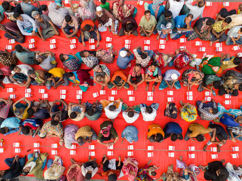 Dhaka, Bangladesh - 17 March 2026: Aerial view of a vibrant gathering of people on a red surface, each person accompanied by a small, neatly placed box.