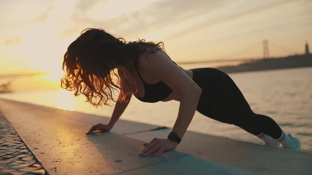Athletic woman doing push-ups outdoor workout at sunset