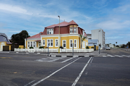 View of a bright yellow colonial-style building with a red roof on a street corner with a white fence under a blue sky in Swakopmund, Erongo Region, Namibia.