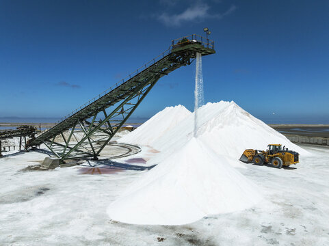 Aerial view of stark white salt piles contrast against the turquoise sky and the machinery at the Walvis Bay Salt Refiners, Walvis Bay, Erongo Region, Namibia.
