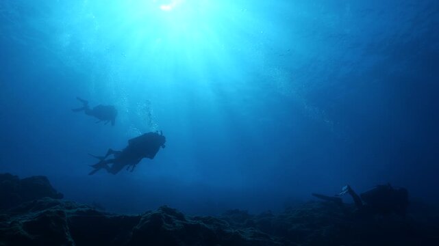 scuba divers exploring underwater with sun beams and rays