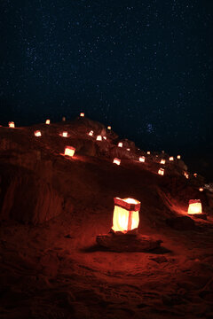 View of glowing paper lanterns placed on a rocky desert slope under a clear starry night sky in Namibia.