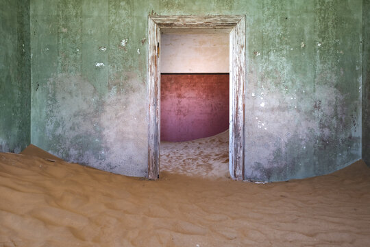 View of an abandoned room filled with desert sand dunes and peeling green walls in Kolmanskop, Karas Region, Namibia.