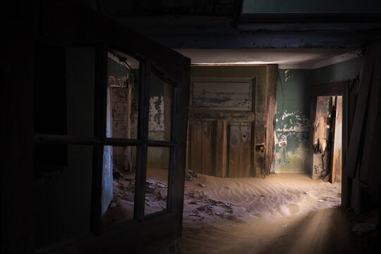 View of the interior of an abandoned house filled with desert sand and peeling green paint on the walls in Kolmanskop, Karas Region, Namibia.