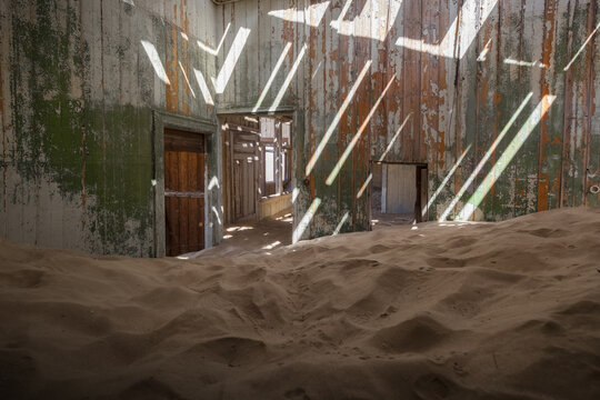View of an abandoned room filled with desert sand and sunlight rays hitting peeling green walls in Kolmanskop, Karas Region, Namibia.