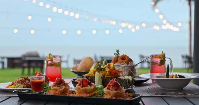 Thai seafood dinner sitting on outdoor table at beachfront restaurant, evening string lights and ocean background, luxury tropical vacation, fine dining, travel lifestyle.