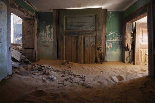 View of the interior of an abandoned house filled with sand dunes and peeling green paint in Kolmanskop, Karas Region, Namibia.
