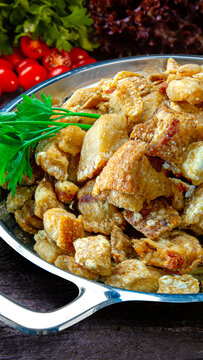 pork rinds (torresmo) fried in ceramic bowl on rustic wooden table in restaurant.