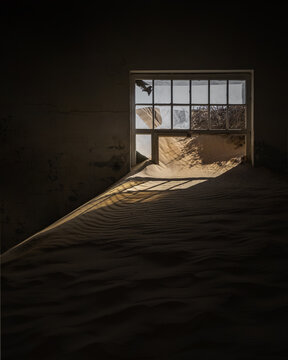 View of sand dunes filling the interior of an abandoned house with light streaming through a broken window in Kolmanskop, Karas Region, Namibia.