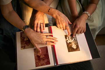Close up of women hands pointing at family photo album, reviewing printed memories and sharing personal history. Suitable for genealogy, family heritage, nostalgia, lifestyle marketing