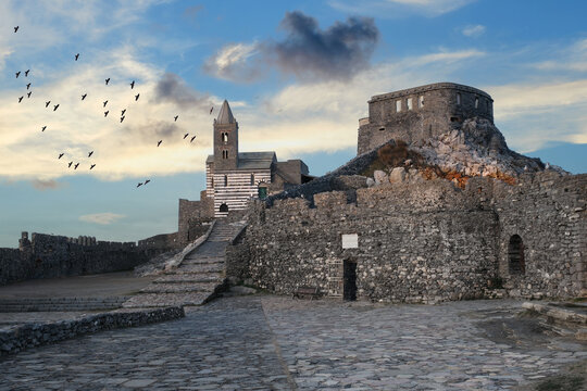 View of the Church of Saint Peter and ancient stone fortifications under a blue sky with birds flying in Porto Venere, Liguria, Italy.