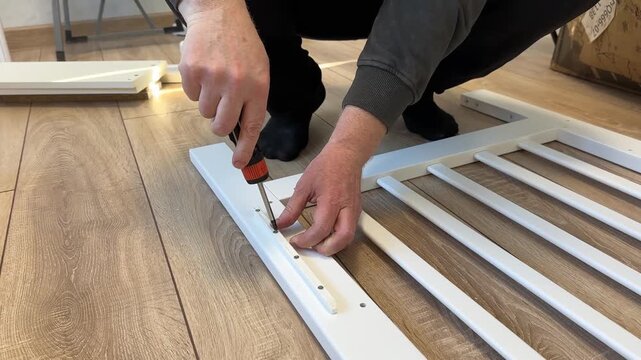 Process of assembling a baby cot. Soft focus. Man screws the side part with a screwdriver. Self-assembly of furniture at home