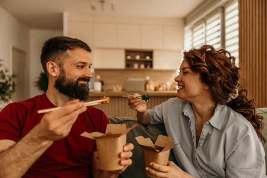 Couple sharing takeout meal with chopsticks at home